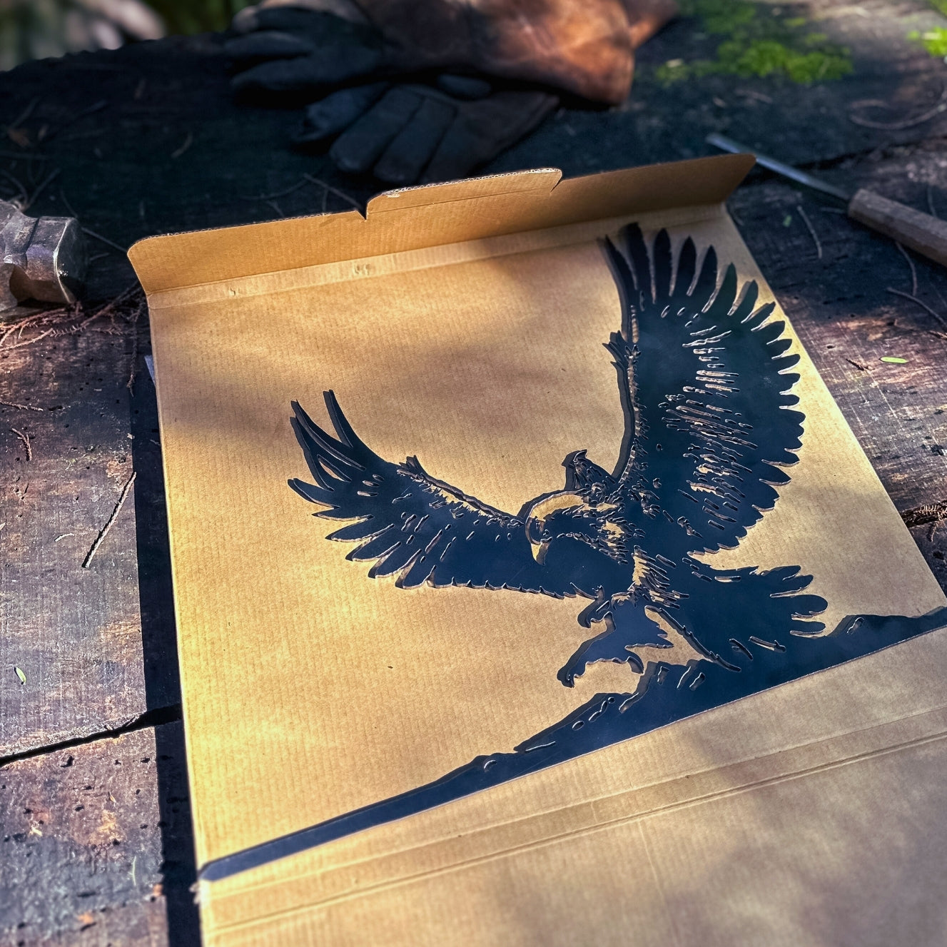 A cardboard box from Metalbird UK lies open on wood, revealing the GANDALF™ ON GWAIHIR™ silhouette—ideal for gifts or unique yard art. Sunlight and work gloves are seen in the background.