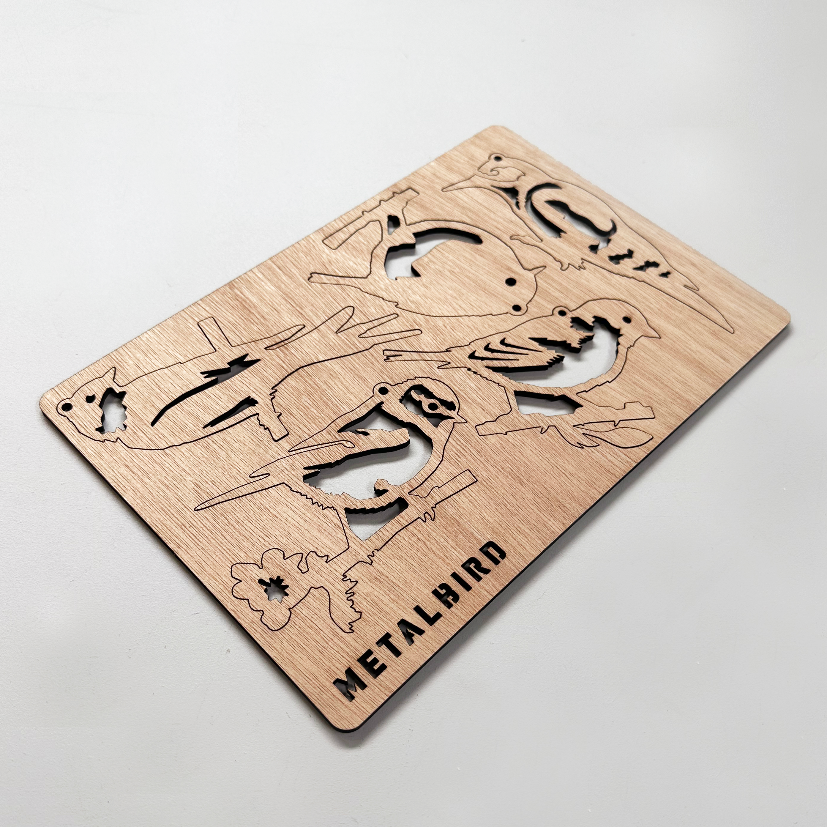 A Wooden Hanging Decoration by Metalbird UK featuring cutouts of various bird shapes and the brand engraved at the bottom, ideal as a unique gift or to inspire your next yard art project, shown on a light-colored surface.