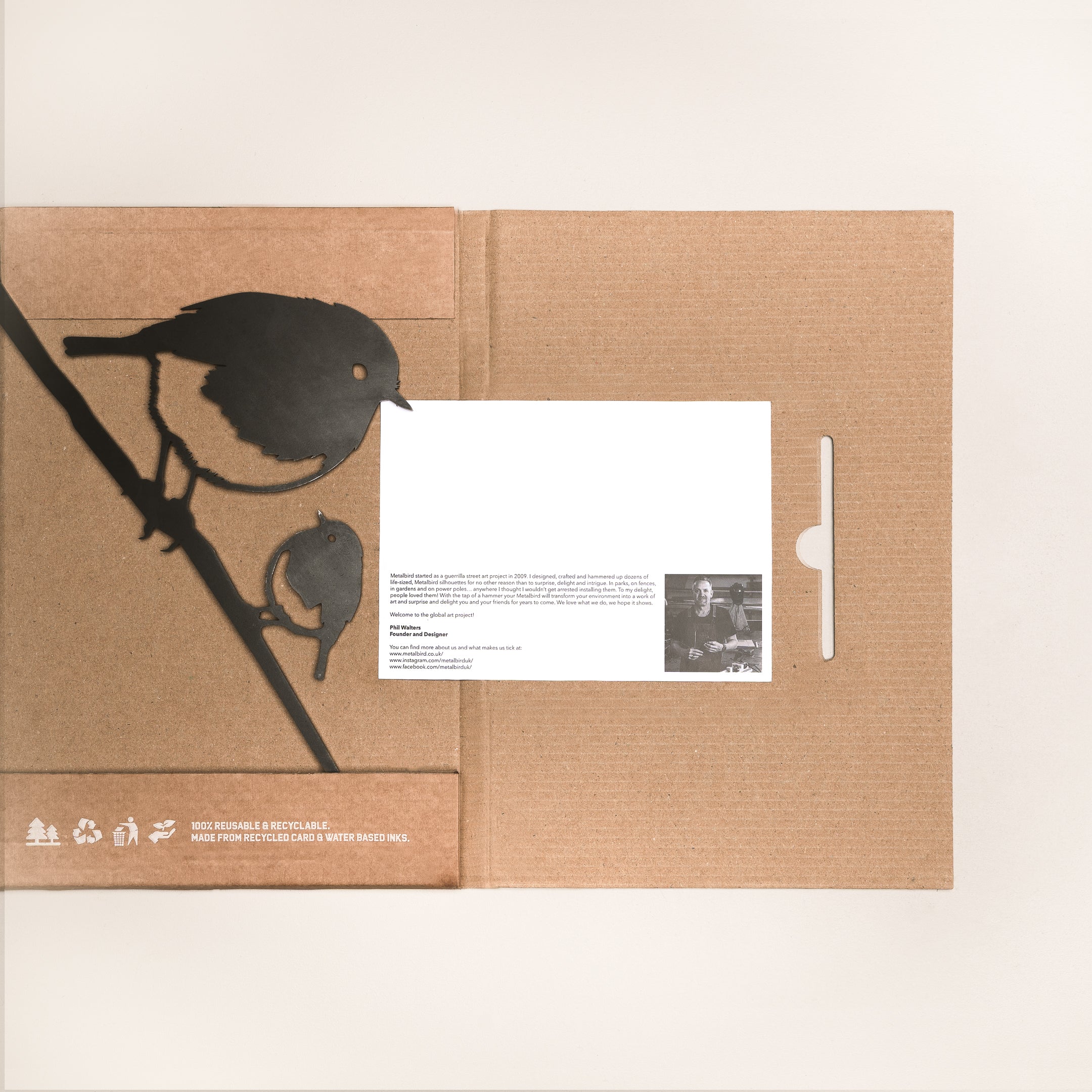 The "Robin and Chick" folder by Metalbird UK features a black illustration of two birds on a branch, inspired by metal yard art. A white card with text and photo peeks from a slot. Recycling symbols appear at the bottom left.