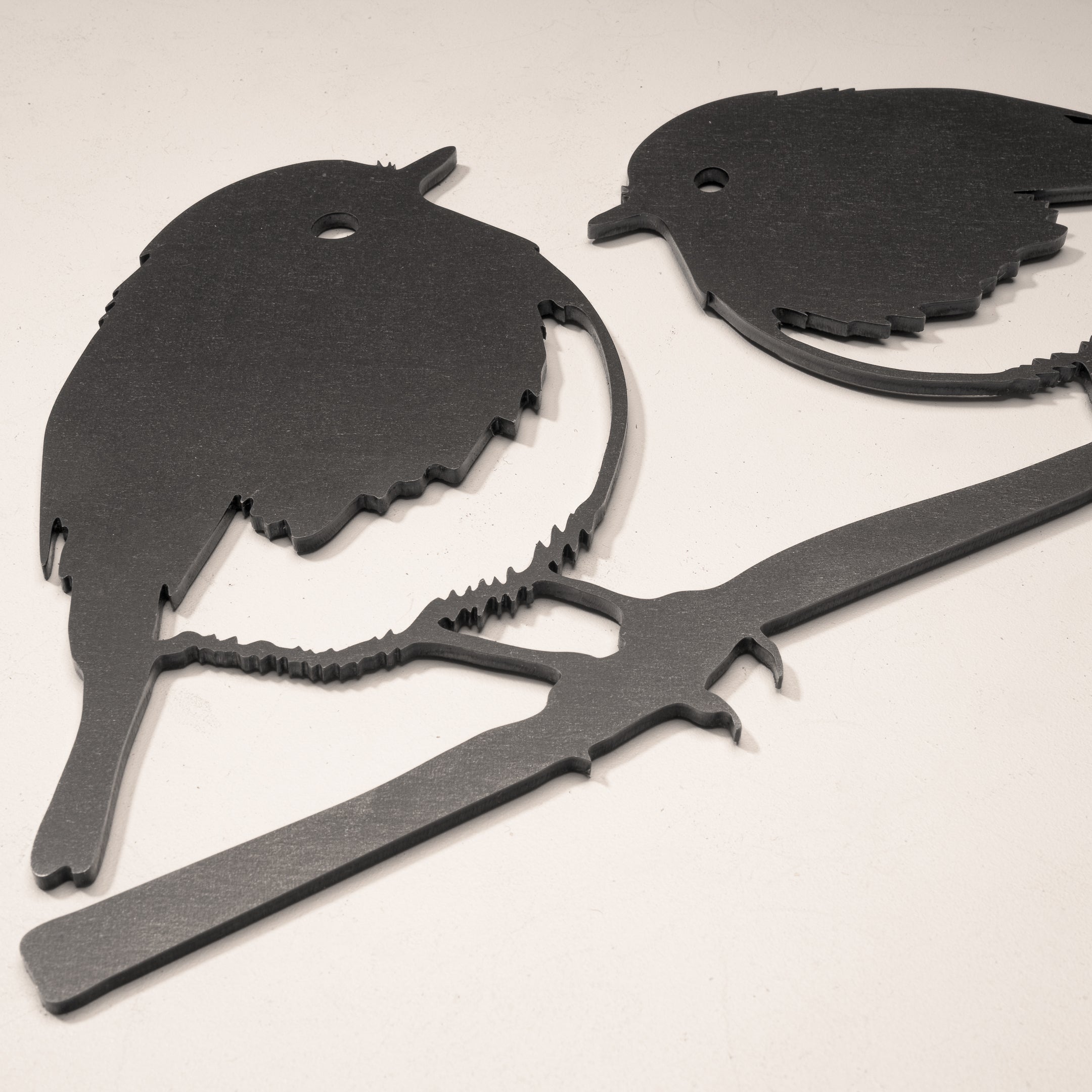 The Robin Pair by Metalbird UK features a black metal silhouette of two birds perched on a branch. With simple cutouts and small holes near the heads, it makes a charming gift or decorative accent for any space.