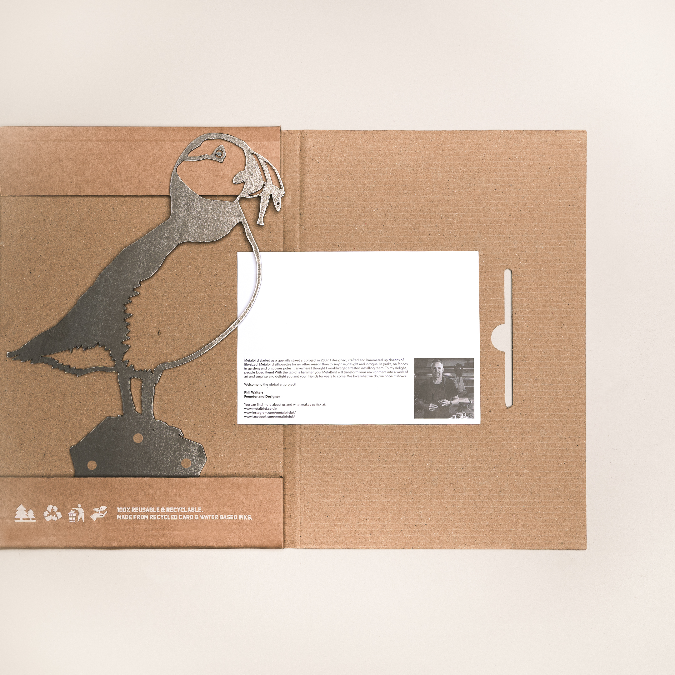 The Puffin by Metalbird UK is a cardboard folder featuring a corten steel puffin silhouette, beside a card with a black-and-white photo and text. The folder displays eco-friendly icons and messaging at the bottom.