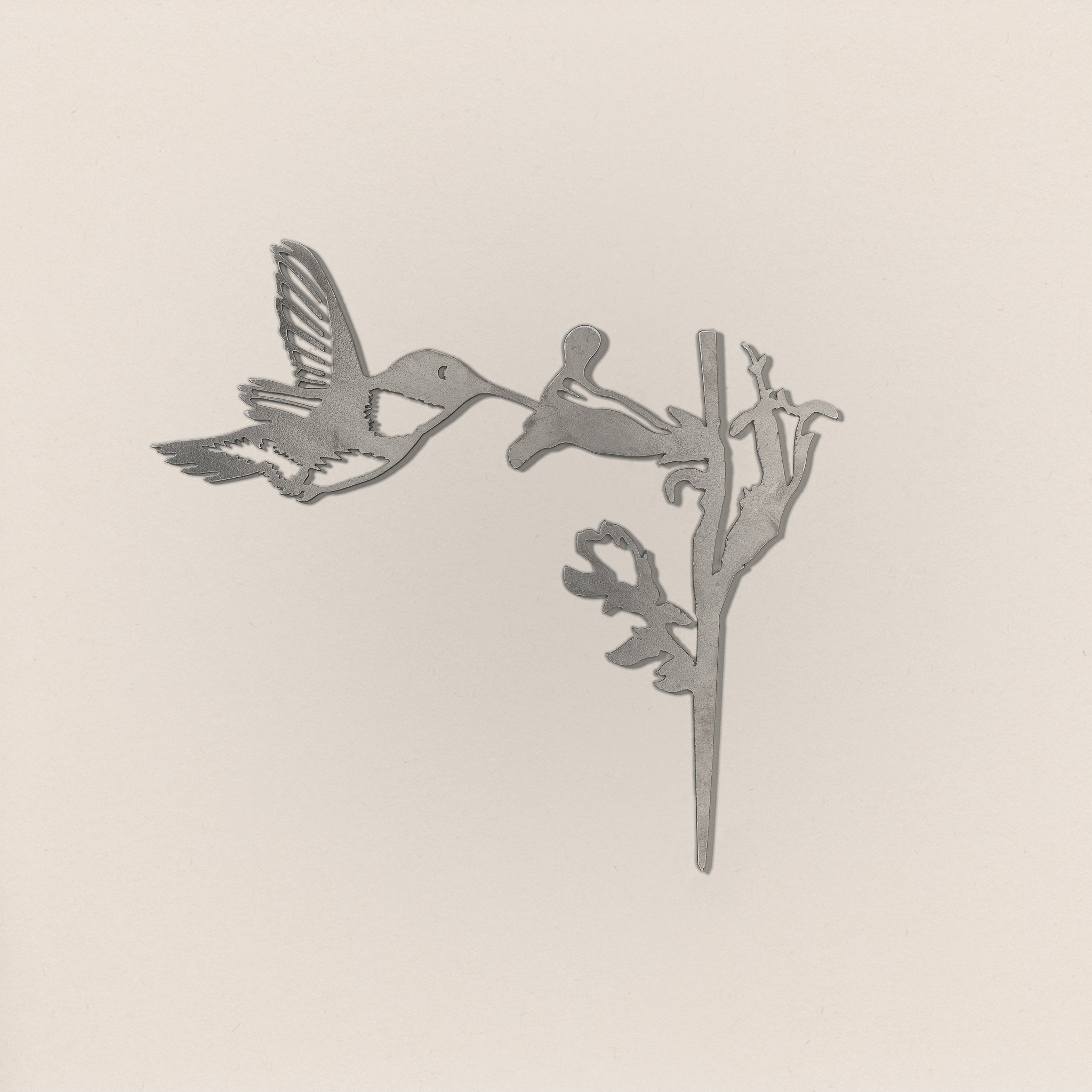 The Hummingbird by Metalbird UK features a grayscale silhouette of a hovering hummingbird beside a flower, set against a light background—ideal as unique garden art or a thoughtful gift.