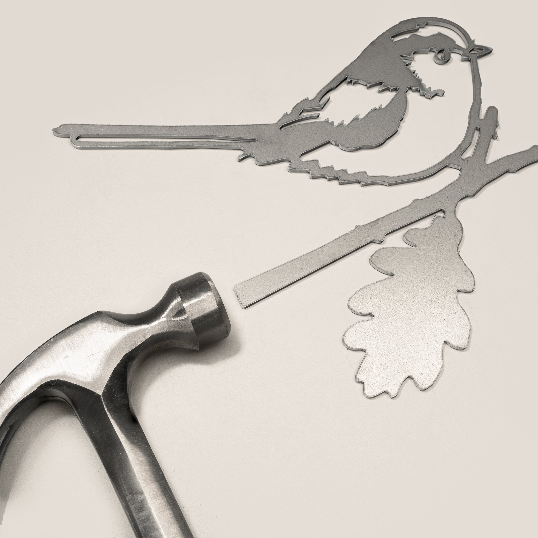 The Metalbird UK Long-tailed Tit features a flat metal bird silhouette perched on an oak branch, with a hammer included for easy installation—perfect as eye-catching yard art or a unique gift.
