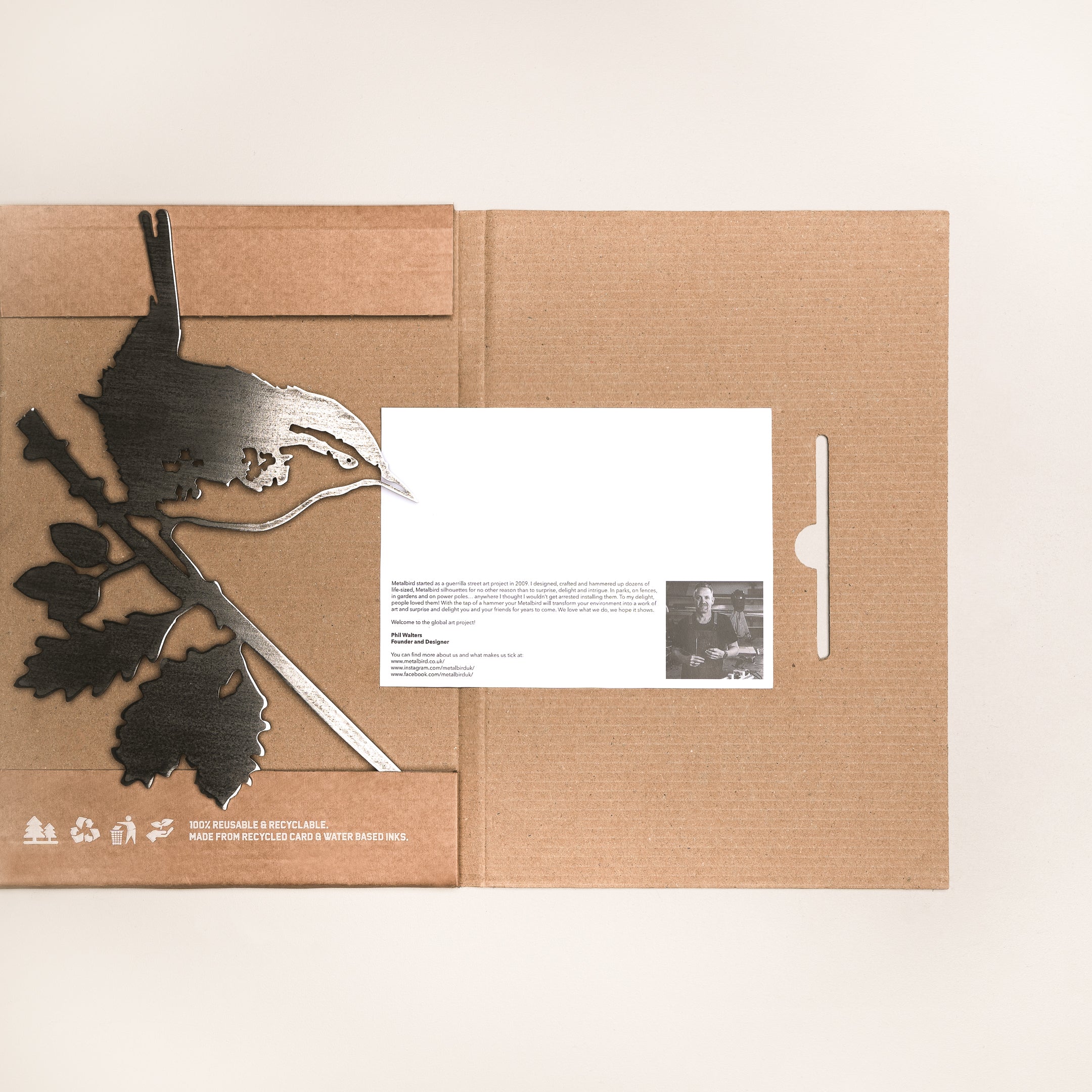 The Wren by Metalbird UK is a metal bird and branch silhouette, packaged in a brown cardboard holder beside an info card with text and a black-and-white photo. Ideal as a gift or yard art, it’s shown against a plain light background.