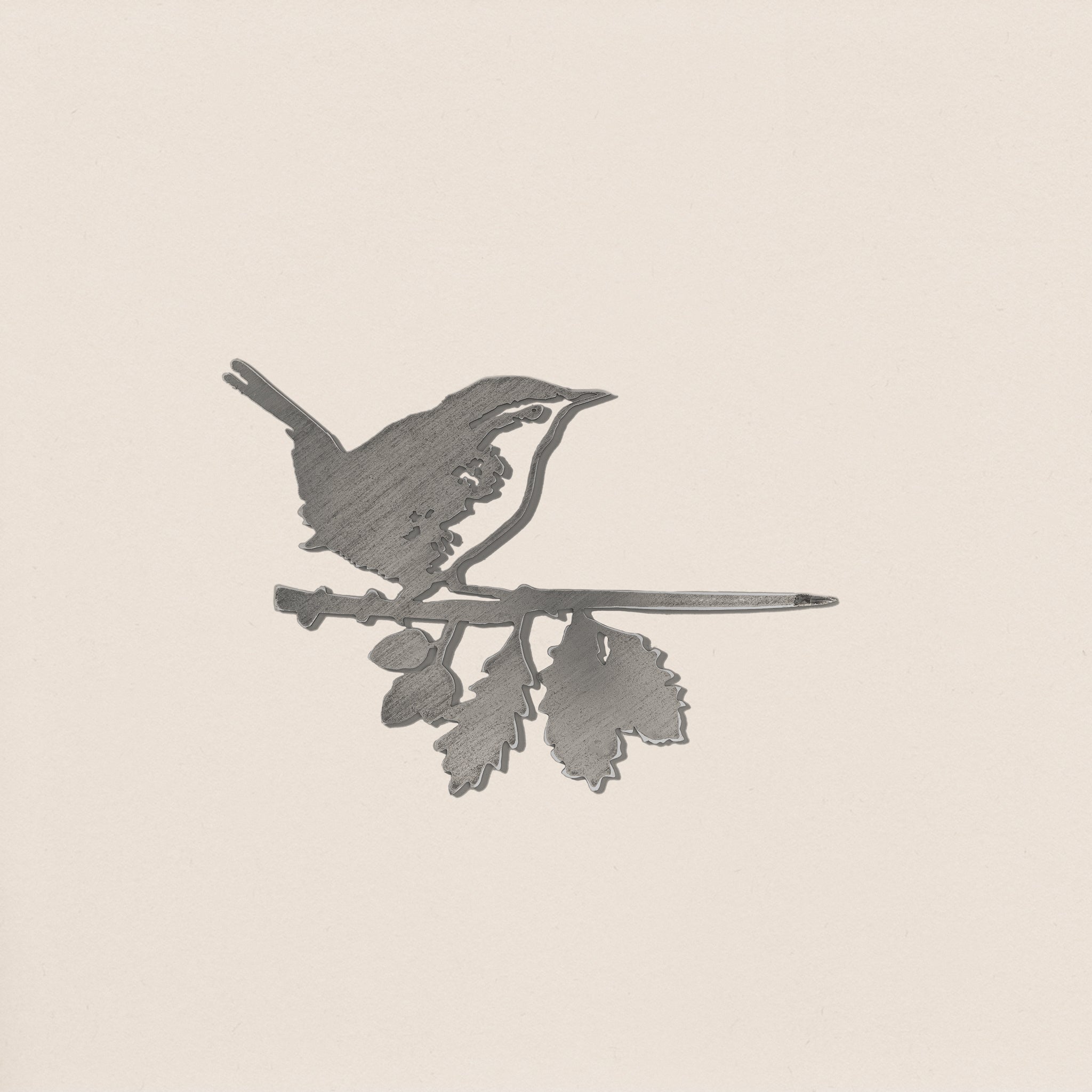 The Metalbird UK Wren is a metal silhouette of a small bird on a leafy branch, set against a light background. Its minimalist design highlights the bird and branch, making it a beautiful and thoughtful gift.