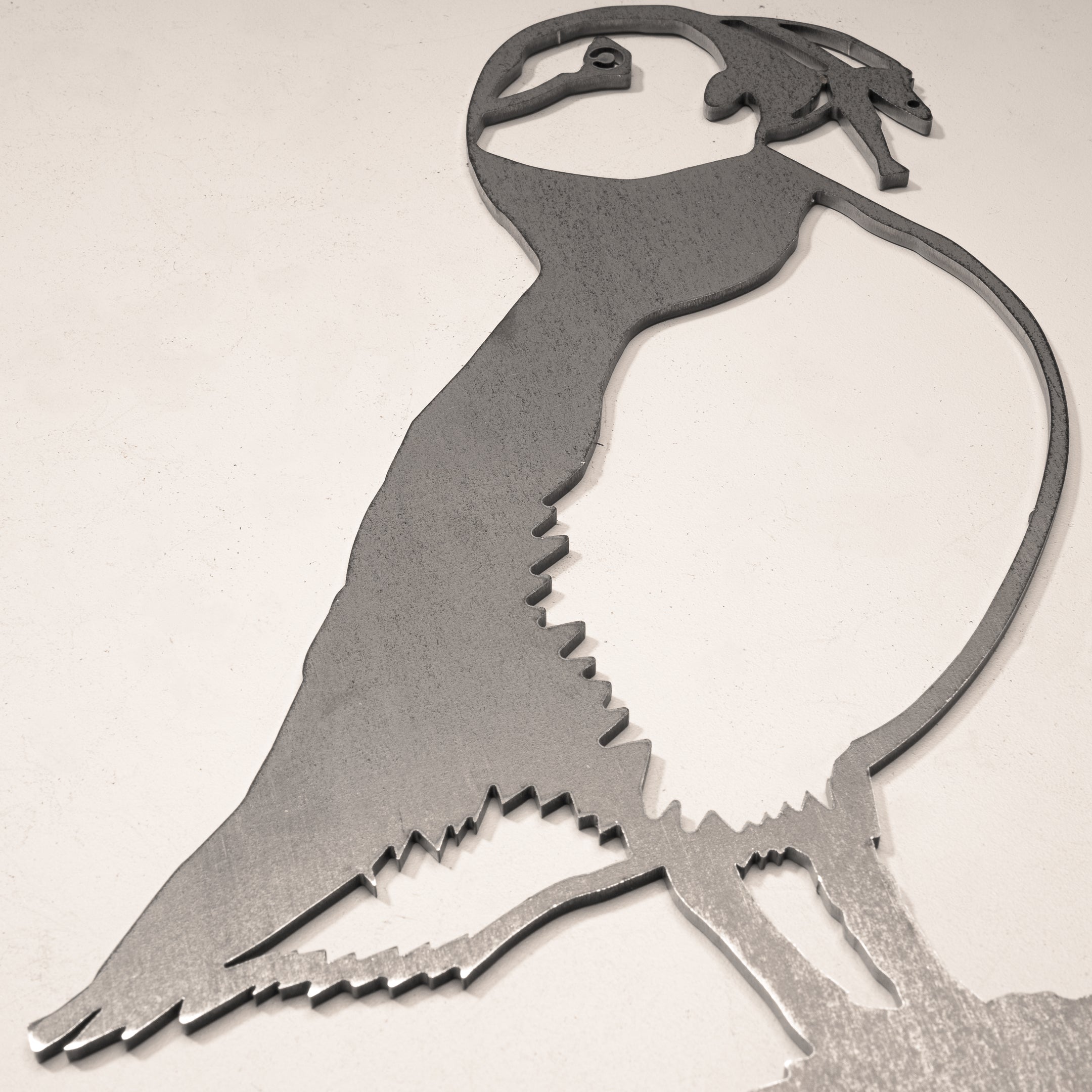 The Metalbird UK "Puffin" is a corten steel silhouette sculpture, depicting the bird in profile with simple, stylized lines, and designed to be mounted against a light-colored wall.