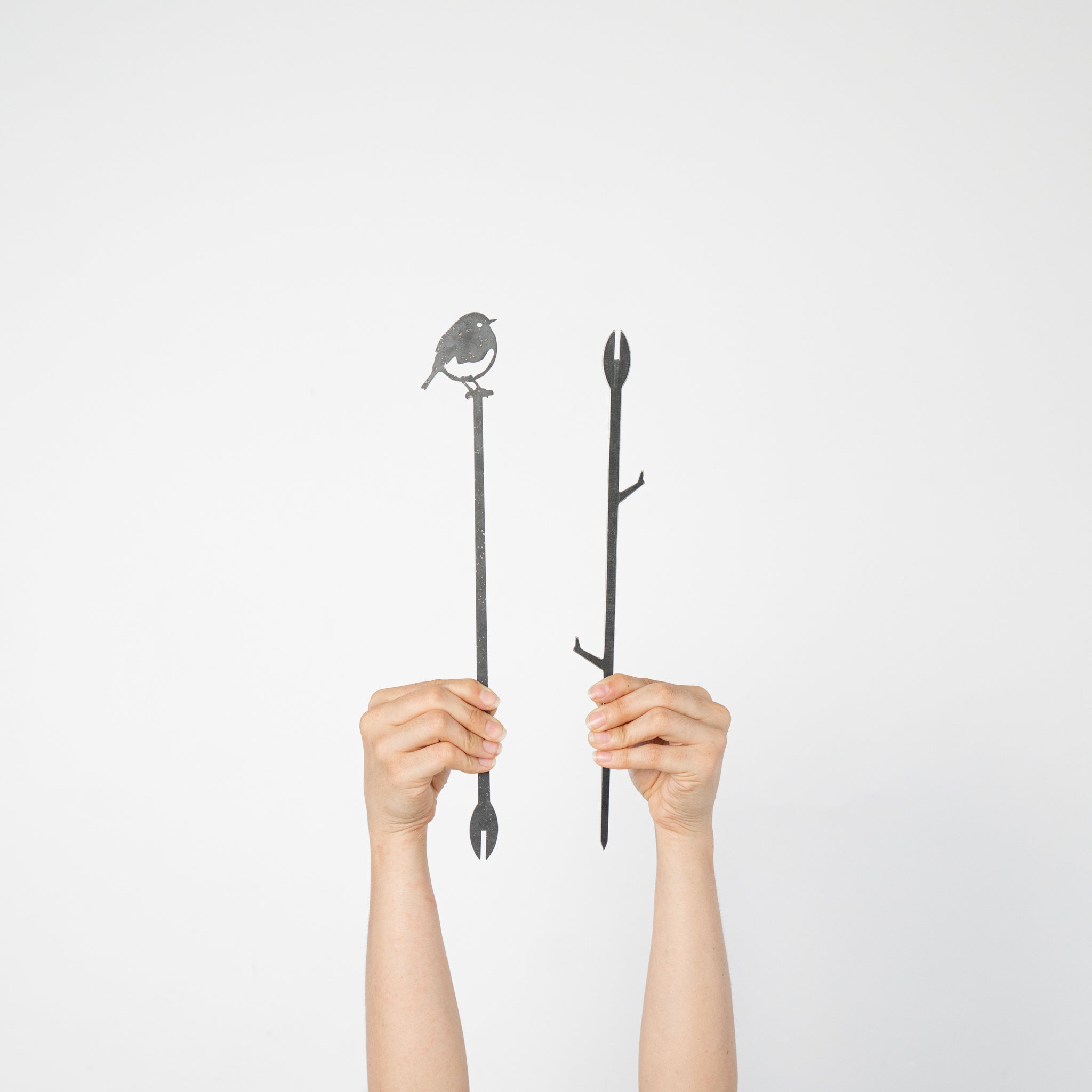 Two hands hold up Metalbird UK's Robin Plant Stake - 70cm against a white background: one features a bird silhouette, the other has branch details—an ideal unique gift or creative accent for your yard art collection.
