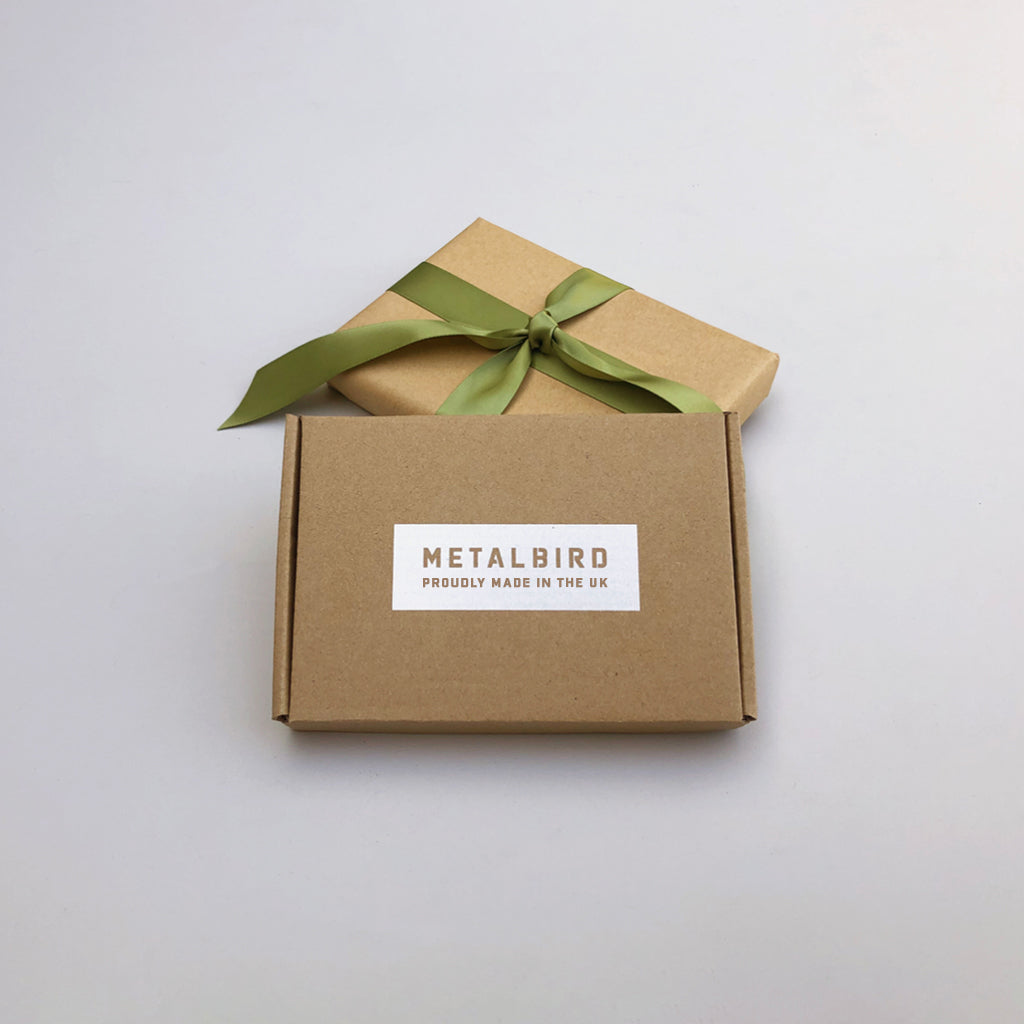 Two brown boxes on a light surface—one with a green ribbon, the other plain and labeled "METALBIRD PROUDLY MADE IN THE UK"—suggest the Baby Bird Bundle by Metalbird UK, unique garden art crafted from premium corten steel.