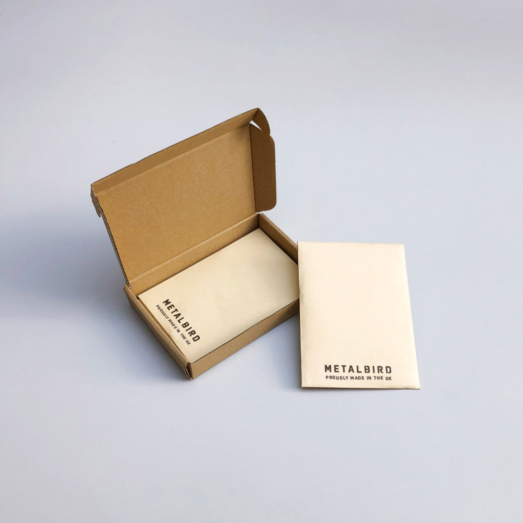 A small open brown cardboard box and a cream-colored envelope, both labeled Metalbird UK, display the Baby Bird Bundle—unique metal garden art—against a plain light background.