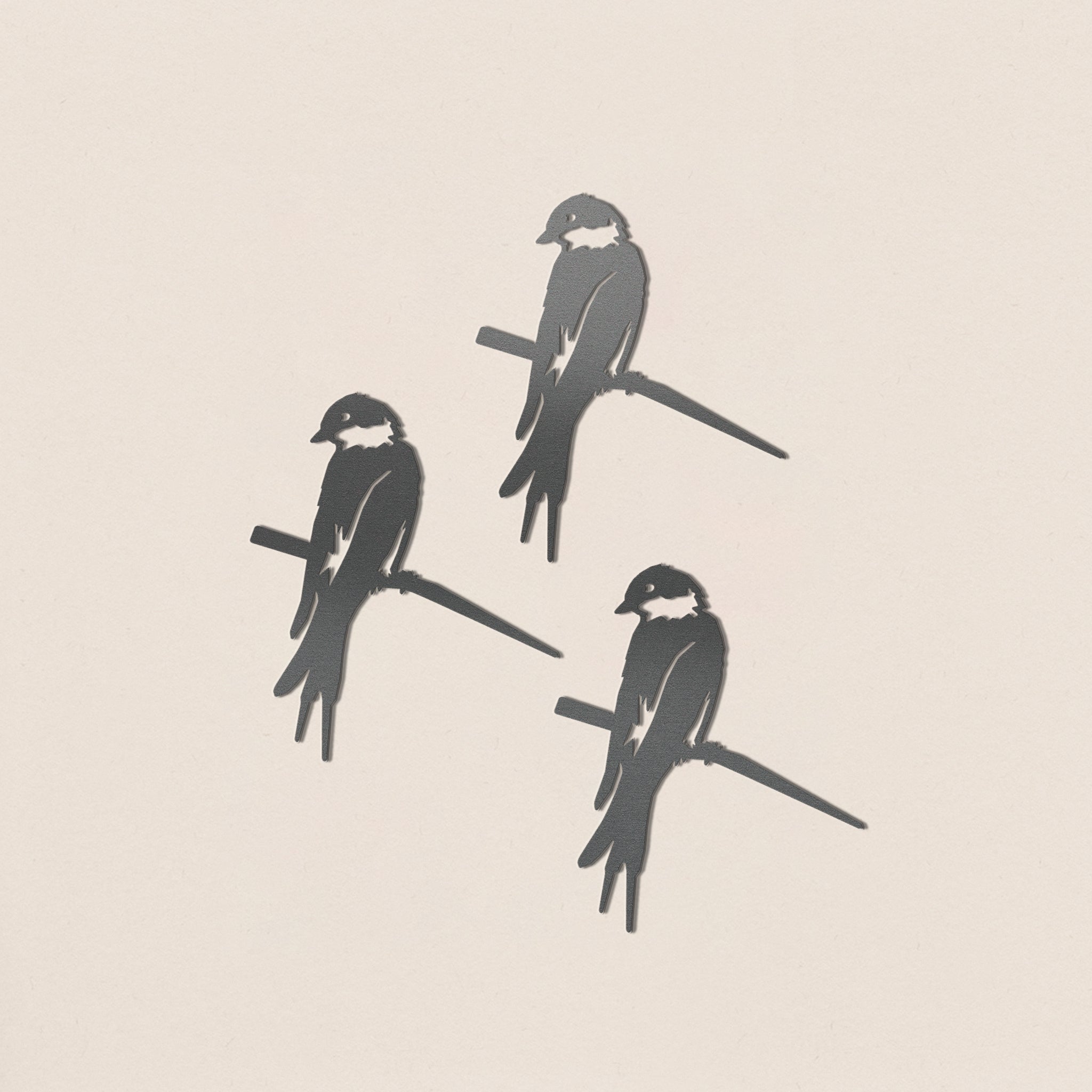 The Baby Bird Bundle - Swallow Trio by Metalbird UK features three stylized black-and-white swallows with white cheeks, perched on branches against a light beige background, evoking corten steel yard art in a loose triangular formation.