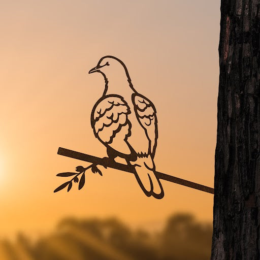 The Metalbird UK "Turtle Dove" is a corten steel silhouette of a bird on a branch, mounted to a tree for unique yard art, with soft orange sunset and sun rays in the background.