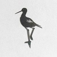 The Metalbird UK "Metalbird Seconds - Black Stilt" features a shorebird silhouette with minor flaws, standing on one leg—ideal as discounted garden bird decor for your white textured wall.