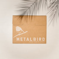 A brown cardboard envelope with a white illustration of an Osprey on a branch, the text METALBIRD UK PROUDLY MADE HERE IN THE UK, and a palm leaf shadow—ideal packaging for this premium corten steel gift by Metalbird UK.