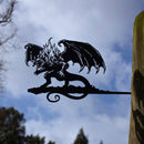 A striking corten steel BALROG™ silhouette by Metalbird UK, featuring wings and flames, is mounted on a wooden post against a cloudy sky with tree branches—an unforgettable gift for any fantasy lover.