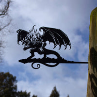 A striking corten steel BALROG™ silhouette by Metalbird UK, featuring wings and flames, is mounted on a wooden post against a cloudy sky with tree branches—an unforgettable gift for any fantasy lover.