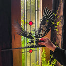 A hand holds the GANDALF™ ON GWAIHIR™ corten steel silhouette by Metalbird UK before a stained glass window with red circular accents, framed by wooden panels and lush green plants.