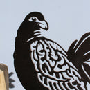 A close-up of Manumea, a premium black metal bird silhouette by Metalbird UK - CC, mounted on a wooden block with intricate cutouts, set against a plain light background—an ideal gift for art lovers.