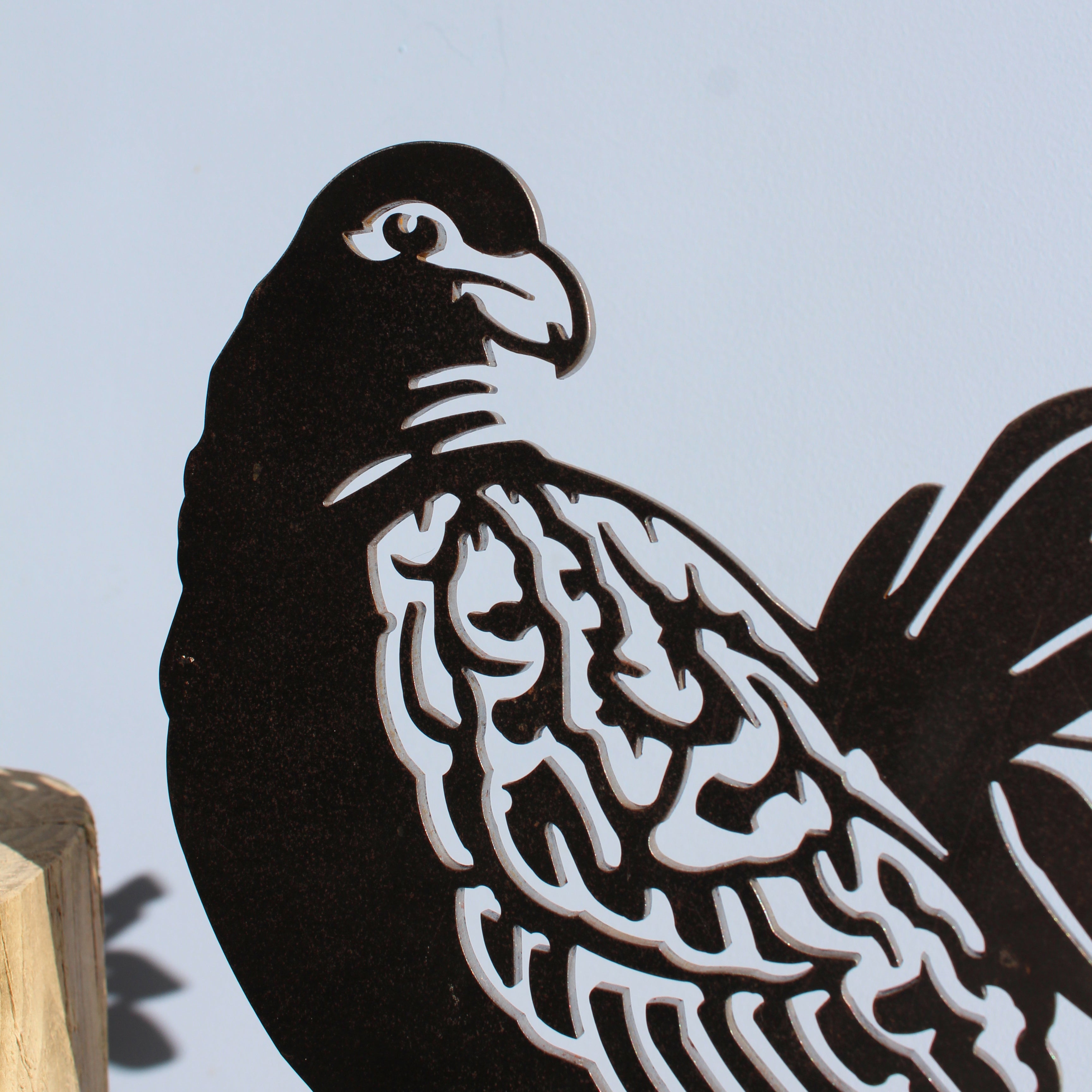 A close-up of Manumea, a premium black metal bird silhouette by Metalbird UK - CC, mounted on a wooden block with intricate cutouts, set against a plain light background—an ideal gift for art lovers.