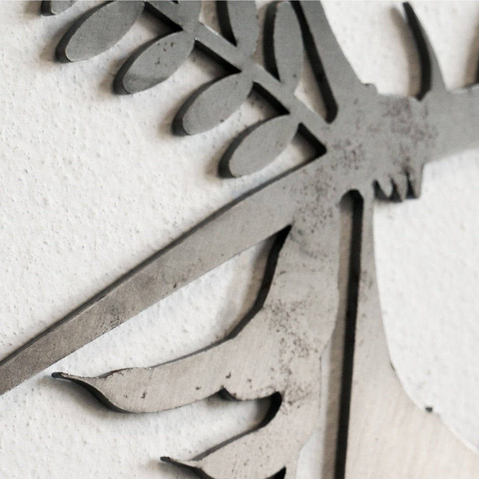 Close-up of the "Blue Tit - Seconds" metal wall art by Metalbird UK, featuring leaf and stem shapes in corten steel with a weathered finish, mounted on a textured white wall.