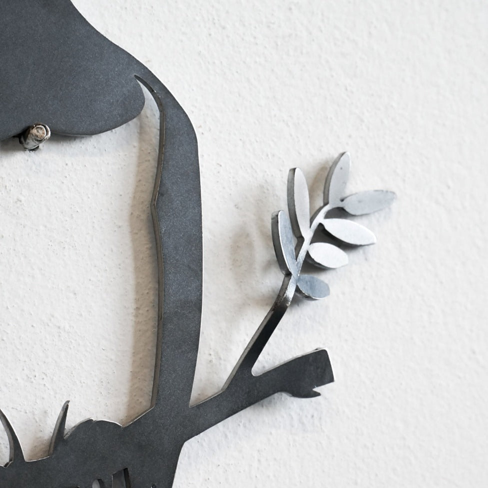 A close-up of the Metalbird Seconds - Robin Pair by Metalbird UK, featuring gray branch, leaves, and subtle metal robin ornaments against a white textured wall. Only part of this discounted garden decor is visible.