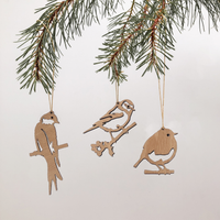 Three Wooden Hanging Decorations by Metalbird UK, each intricately cut from thin wood in unique bird silhouettes, hang from string on a pine branch against a plain white background, capturing the delicate charm of various birds.