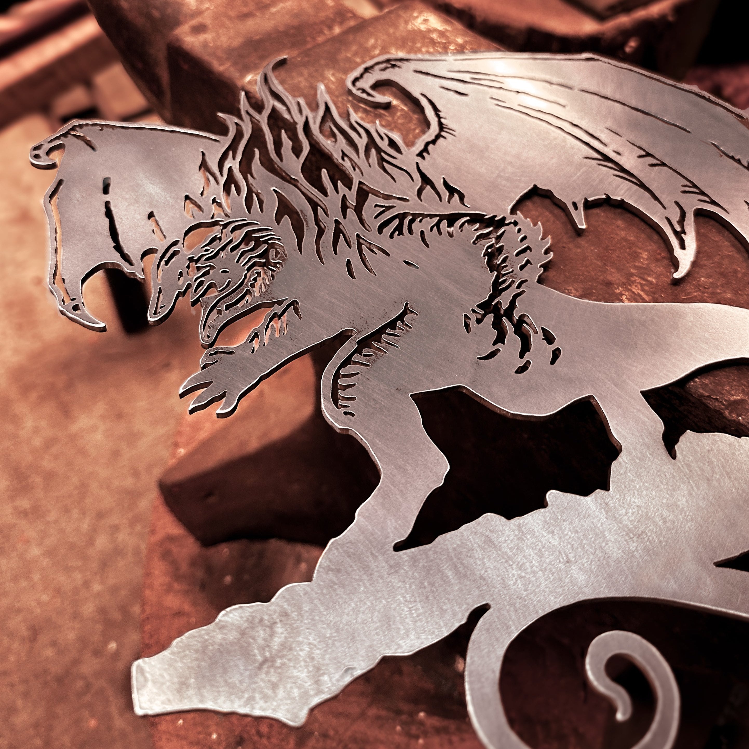 The BALROG™ by Metalbird UK features a corten steel dragon silhouette with detailed wings and a fierce expression, resting on a workbench—artisanally crafted and perfect as a unique gift.