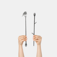 Two hands hold up the Pair Of Plant Stakes by Metalbird UK: one with a perched bird on top, the other with branch-like details—unique yard art accents—shown against a plain white background.