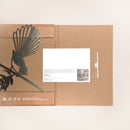 The Fantail (Piwakawaka) by Metalbird UK is a cardboard folder featuring a metal bird on a branch, reminiscent of yard art. A white card with text and photo peeks out on the right, set against a neutral background.