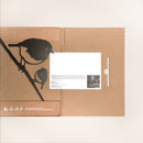 The "Robin and Chick" folder by Metalbird UK features a black illustration of two birds on a branch, inspired by metal yard art. A white card with text and photo peeks from a slot. Recycling symbols appear at the bottom left.