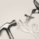 A metal hammer rests beside intricately cut corten steel shapes—a hummingbird, a flower, and branches—on a light surface. The "Hummingbird" by Metalbird UK makes an inspiring gift for metal art enthusiasts.