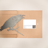 The Metalbird UK "Raven" features a metal garden art raven silhouette on a cardboard folder's left side, with a white card displaying printed text and a small black-and-white photo on the right.