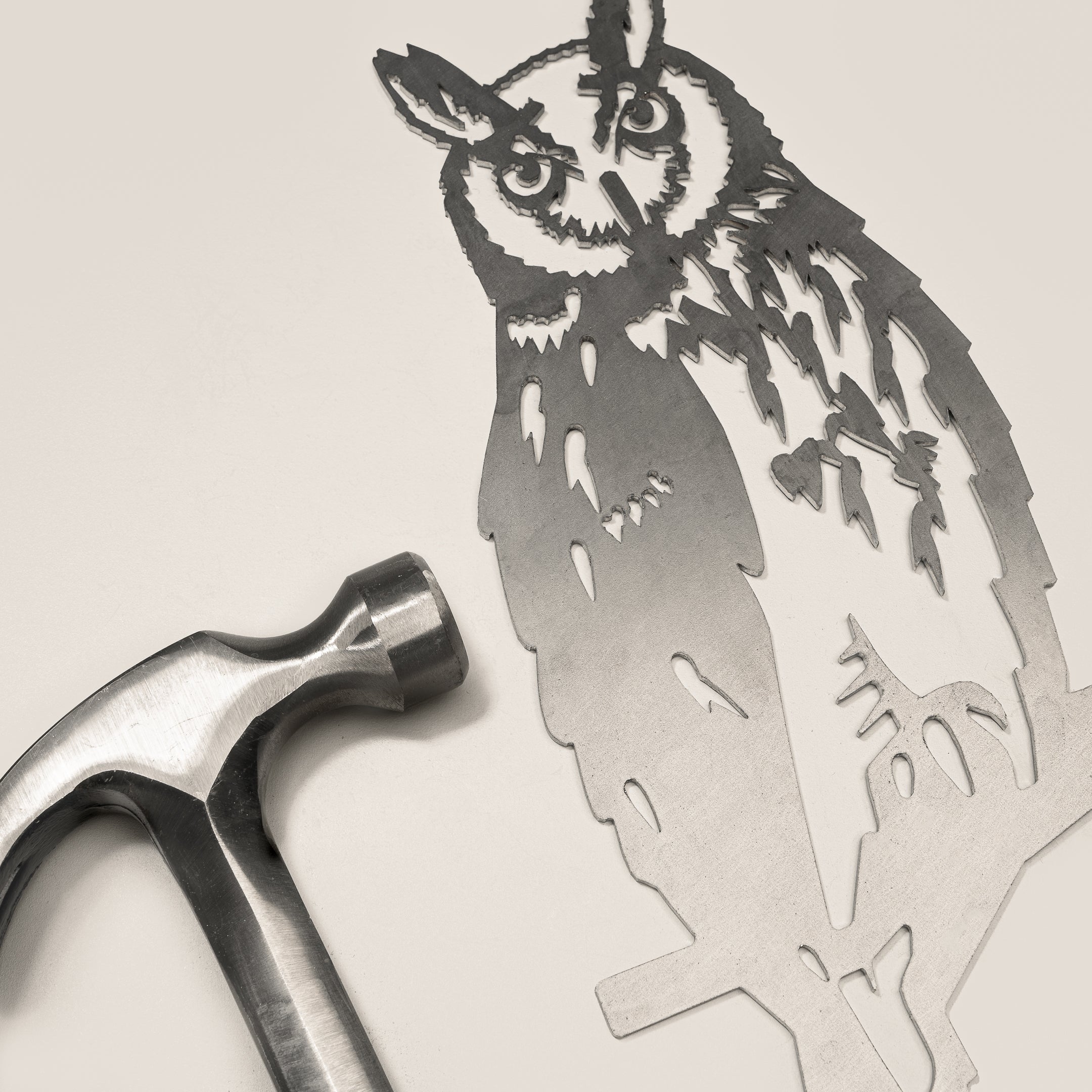 The Metalbird UK Long-eared Owl metal silhouette rests on a light surface beside a steel hammer, evoking DIY or metalworking vibes—an ideal piece for creative outdoor yard art.