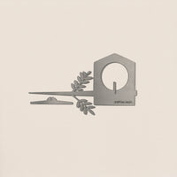 The Metalbird UK Bird Feeder—a minimalist silver metal house with a circular opening, flat strip, and leafy branch—makes an elegant piece of garden art, shown here on a plain off-white background.