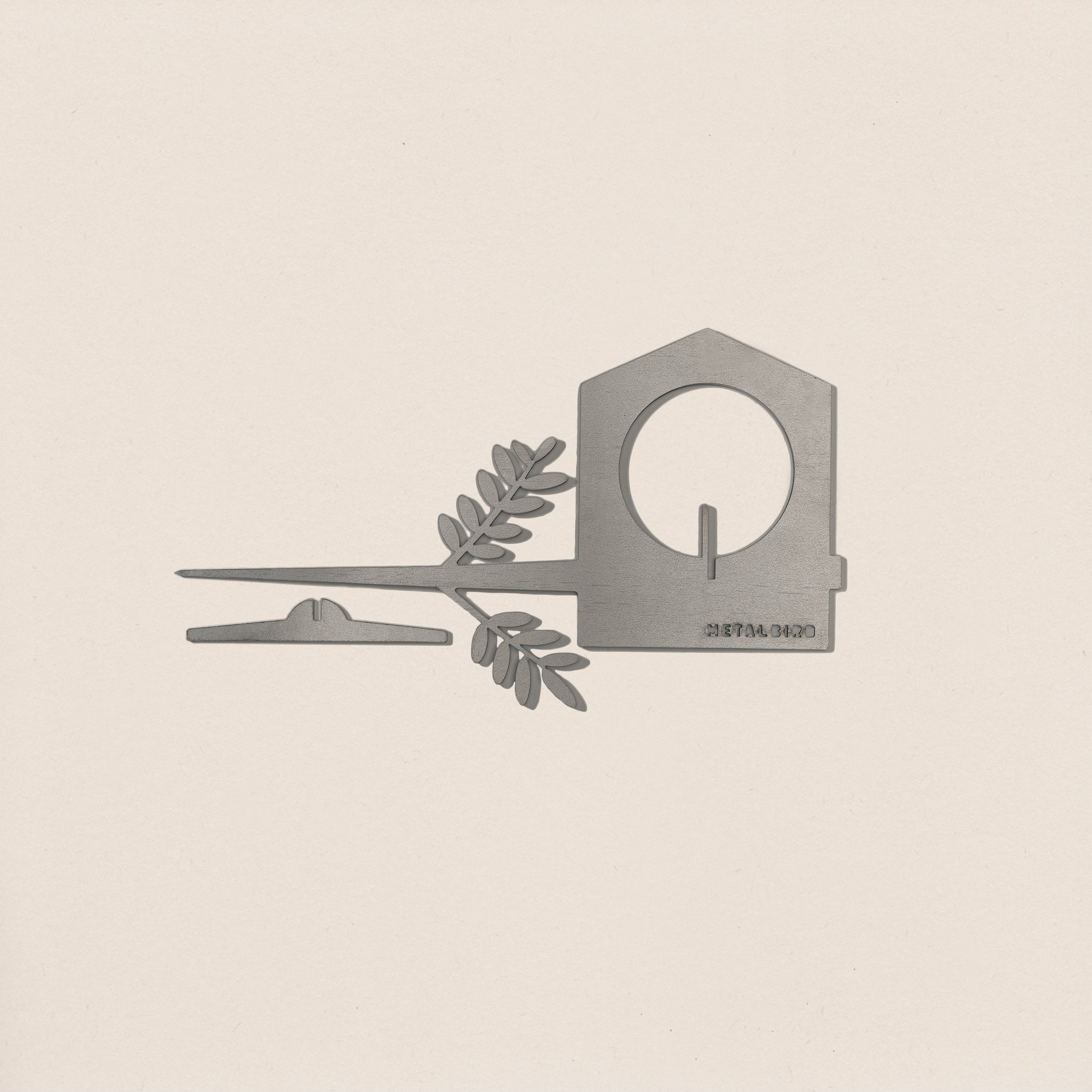 The Metalbird UK Bird Feeder—a minimalist silver metal house with a circular opening, flat strip, and leafy branch—makes an elegant piece of garden art, shown here on a plain off-white background.