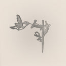 The Hummingbird by Metalbird UK features a grayscale silhouette of a hovering hummingbird beside a flower, set against a light background—ideal as unique garden art or a thoughtful gift.