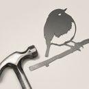 The Metalbird UK Robin, a metal silhouette of a bird perched on a branch, lies next to a metal hammer—perfect as unique yard art or a thoughtful gift—set against a plain background.