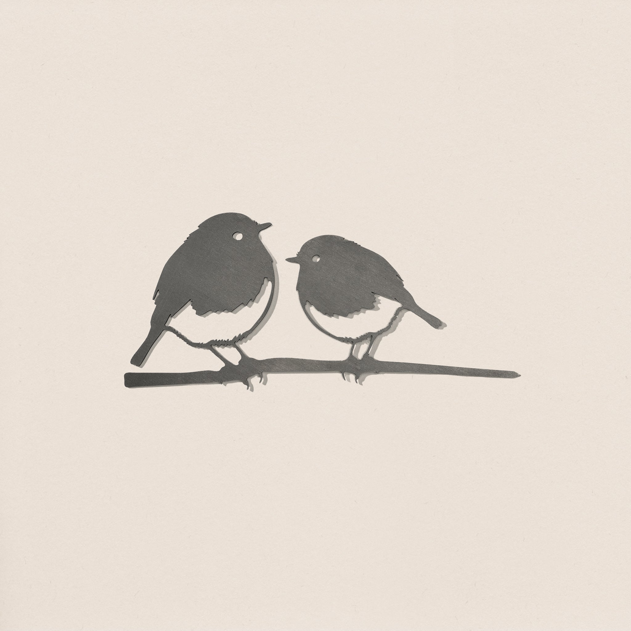 The Robin Pair by Metalbird UK features a simple black and white illustration of two small birds facing each other on a thin branch, evoking garden art, set against a plain light background.