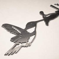 The Hummingbird by Metalbird UK is a metal wall art piece depicting a hummingbird drinking nectar, ideal as garden art and stunning when displayed on a light-colored textured surface.