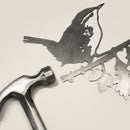 A metal hammer lies next to the Wren decorative silhouette by Metalbird UK, showing a bird perched on a leafy branch, all arranged on a light-colored surface.