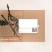 A flat-lay of Metalbird UK's "Long-tailed Tit & Chick" brown cardboard envelope, featuring a metal bird and leaf ornament—ideal for garden art or gifting—alongside a black pen and eco-friendly white card with printed text and photo.