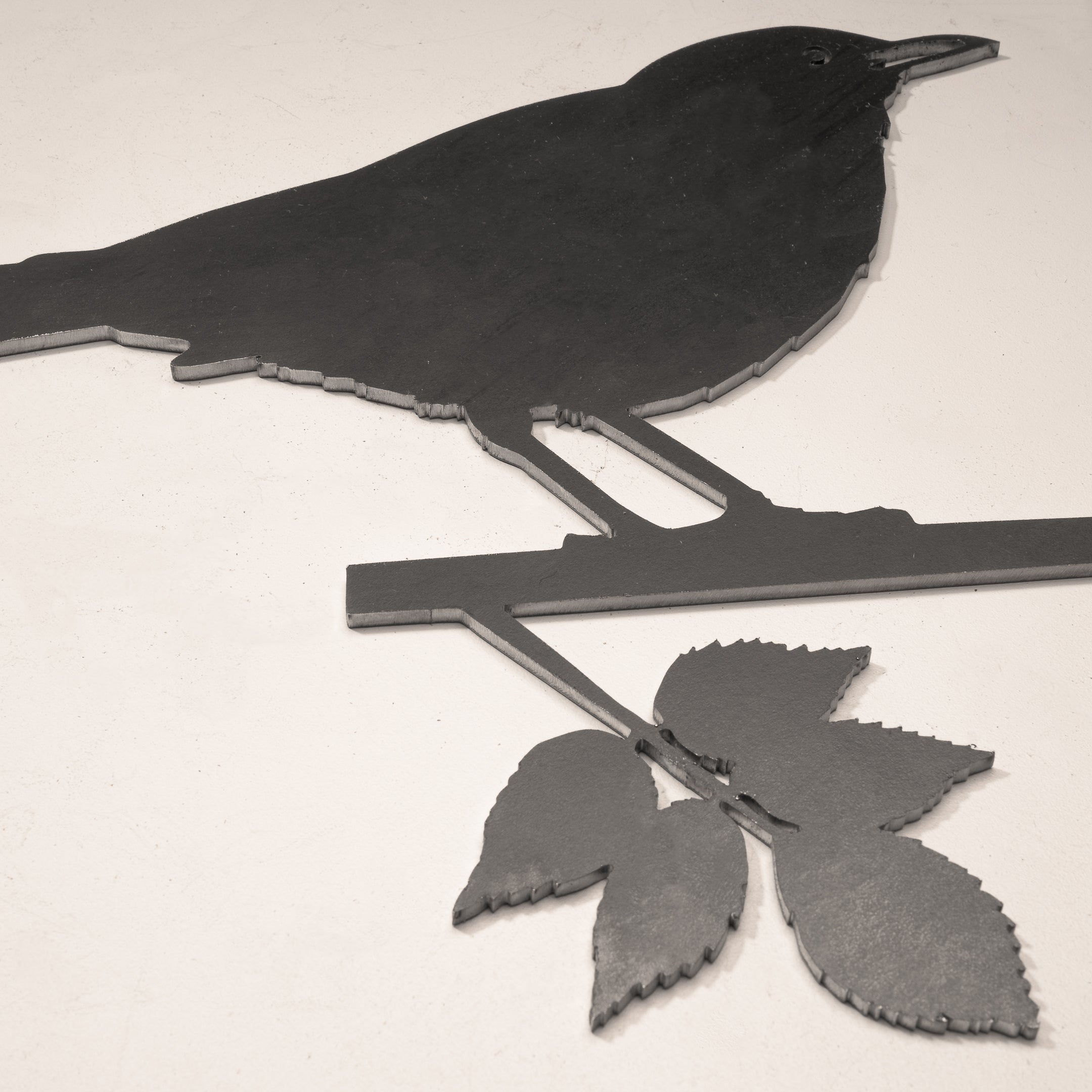 The Blackbird by Metalbird UK is a corten steel silhouette of a bird on a leafy branch, designed to mount on any light wall—a striking yard art piece for your outdoor space.