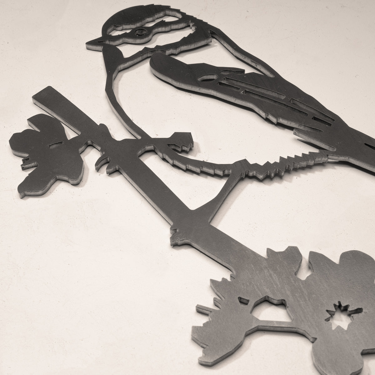 Close-up of the Blue Tit’s cut-steel head, wing and leafy branch.