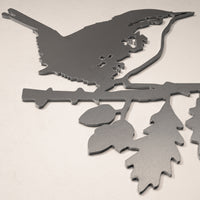 The Metalbird UK Wren is a minimalist, flat corten steel silhouette showing a wren perched on a leafy branch in profile, displayed on a light-colored surface.