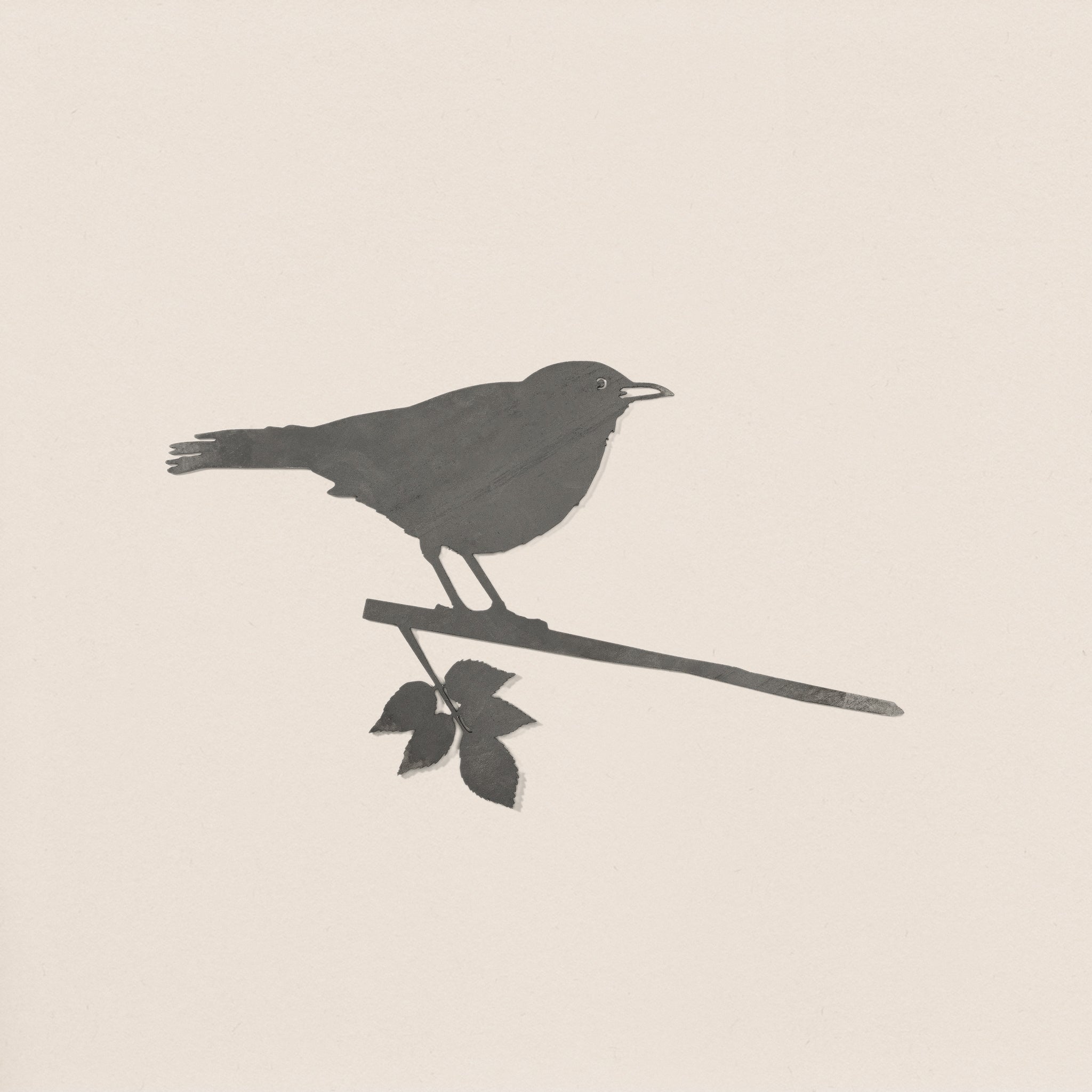 Blackbird by Metalbird UK features a sleek black silhouette of a small bird perched on a leafy branch against an off-white background—an ideal garden art piece or thoughtful gift for nature lovers.