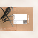 The "Pair of Swallows" by Metalbird UK is a brown cardboard folder featuring two birds on branches, ideal for garden art lovers, with recycling and eco-friendly icons in the corner and partially covering a white card with text and photo.