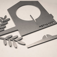 A gray corten steel Bird Feeder by Metalbird UK, featuring a house-shaped frame with circular cutout, two leaf-shaped parts, and a flat rectangle, is arranged on a light surface. Each feeder is engraved with the Metalbird brand.