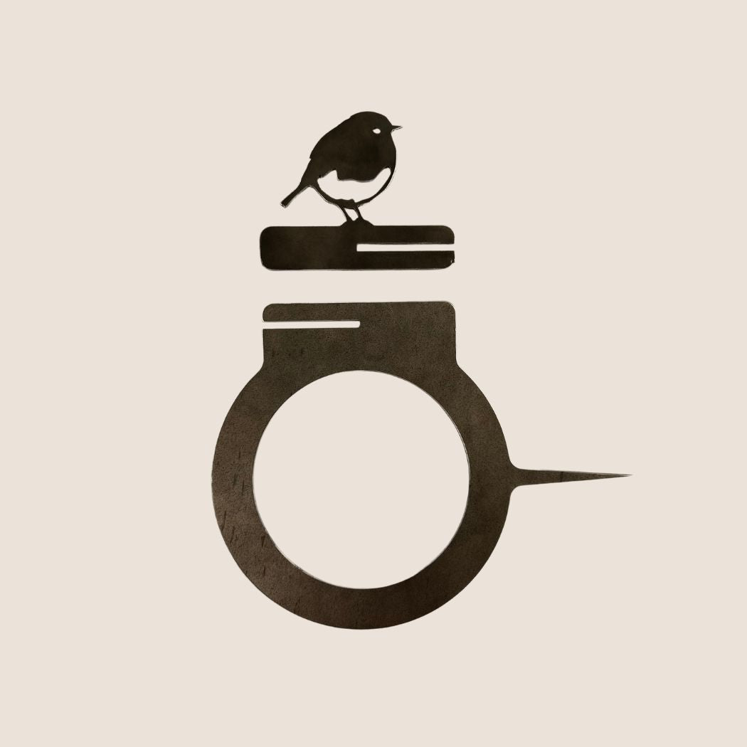 The Bowl Bird Feeder by Metalbird UK features a minimalist black bird on two stacked books, crafted from corten steel and set atop a circular ring—an ideal unique metal gift for any setting.