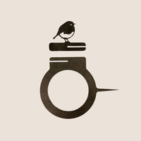 The Bowl Bird Feeder by Metalbird UK features a minimalist black bird on two stacked books, crafted from corten steel and set atop a circular ring—an ideal unique metal gift for any setting.