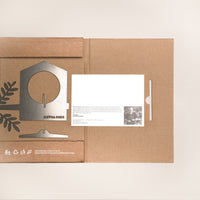 An open cardboard package from Metalbird UK holds a flat metal Bird Feeder kit, a white instruction card, and leaf cutouts on a light background—the perfect eco-friendly gift for garden art lovers.
