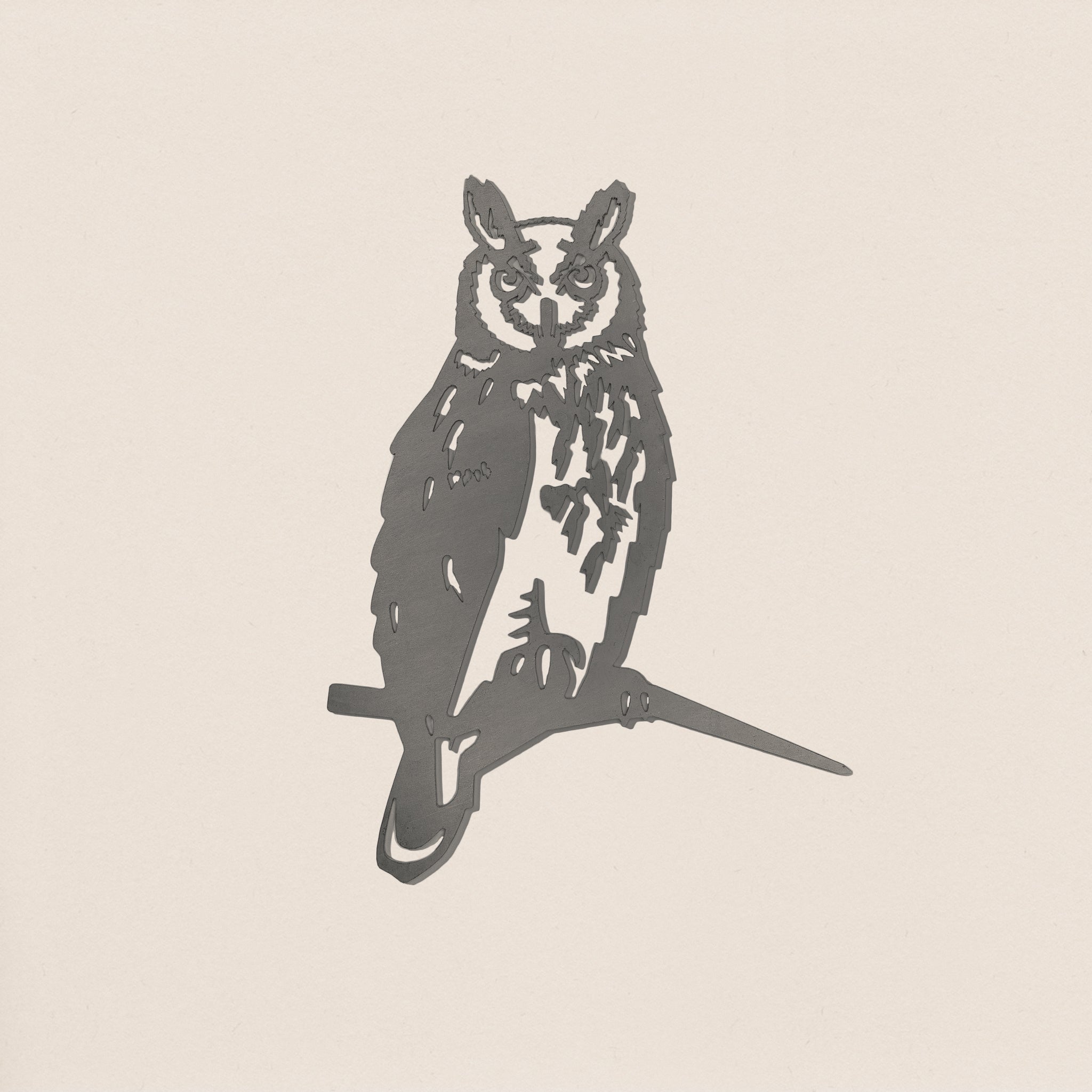 The Metalbird UK Long-eared Owl is a minimalist black corten steel silhouette of an owl perched on a branch, displayed against a plain off-white background.